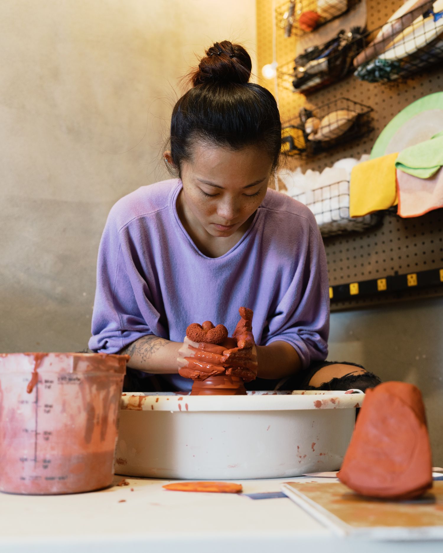 Woman in purple sweater shaping red clay on a pottery wheel in an art studio.
