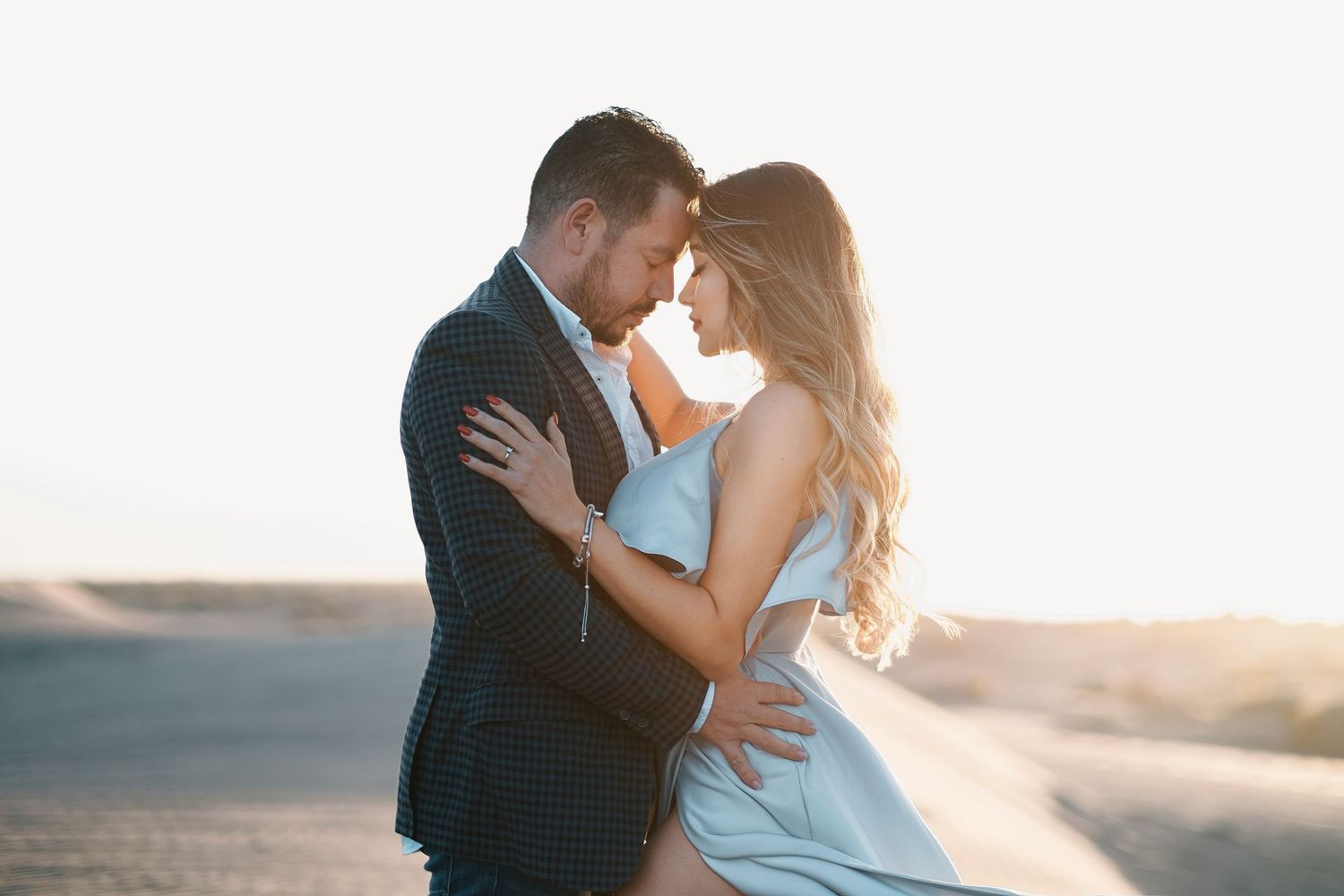 Romantic couple embracing at sunset in a desert landscape, man in suit and woman in elegant dress.