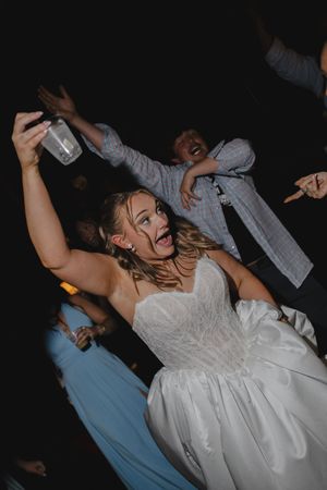 Bride in white strapless gown celebrates energetically on the dance floor at her wedding reception.