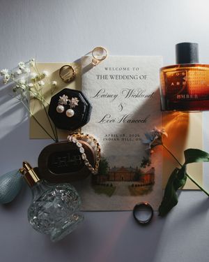 Elegant wedding flat lay featuring invitation, pearl earrings, gold bracelet, perfume bottles, and floral accents for Lainey and Levi.