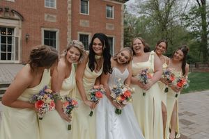 Bride and bridesmaids in yellow dresses laughing together outdoors holding colorful bouquets at a brick estate wedding.