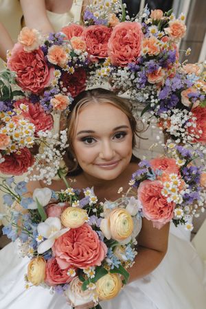 Bride framed by colorful wedding bouquets featuring coral peonies, purple flowers, daisies, and ranunculus.