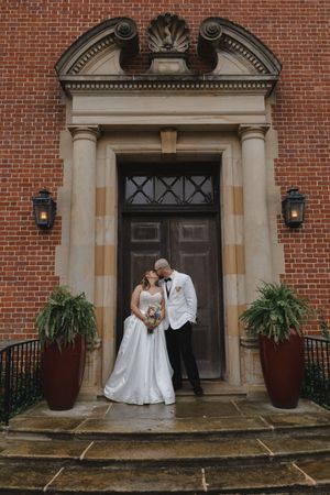 Bride and groom share a romantic moment at the ornate entrance of a red brick wedding venue.