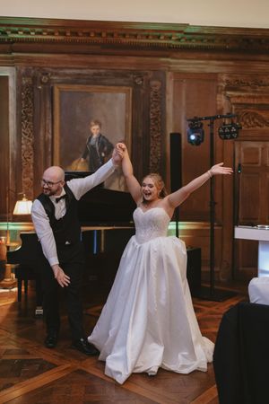Bride and groom make grand entrance into elegant wood-paneled reception hall with grand piano.