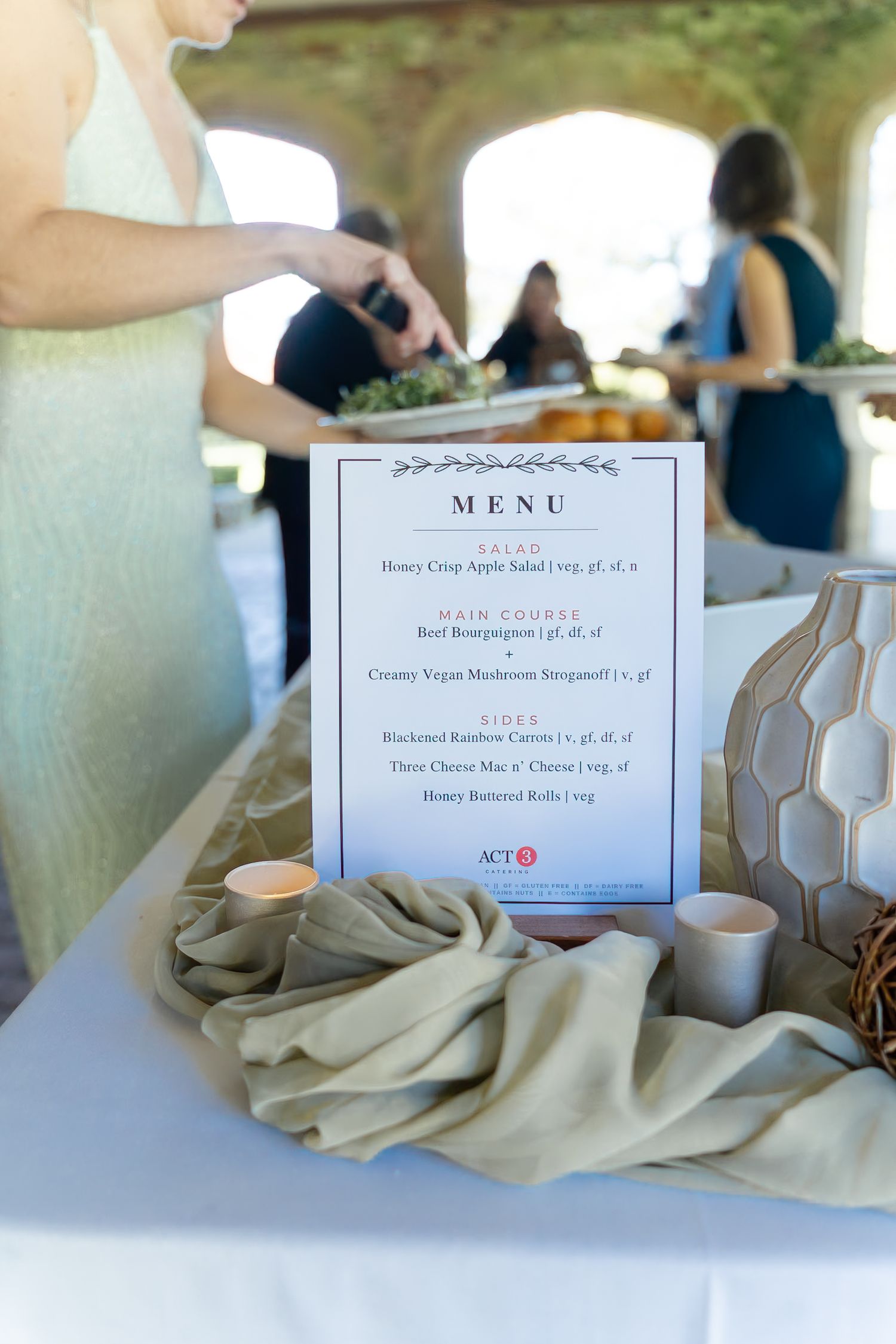Elegant wedding reception menu display on a draped table with candles, featuring salad, main course, and sides options.
