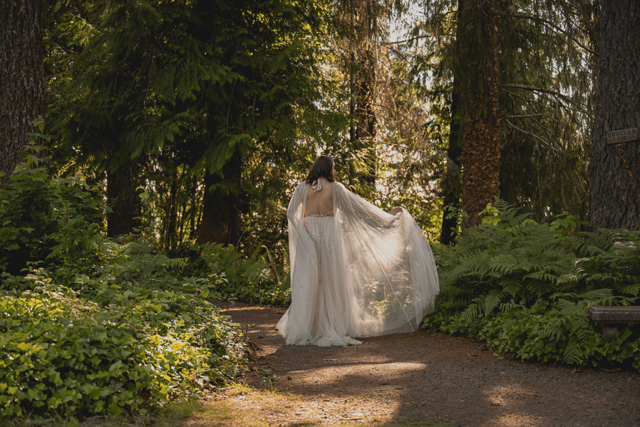 A bride plays with the fabric of her dress in a patch of sunlight on a forested path in Washington state.