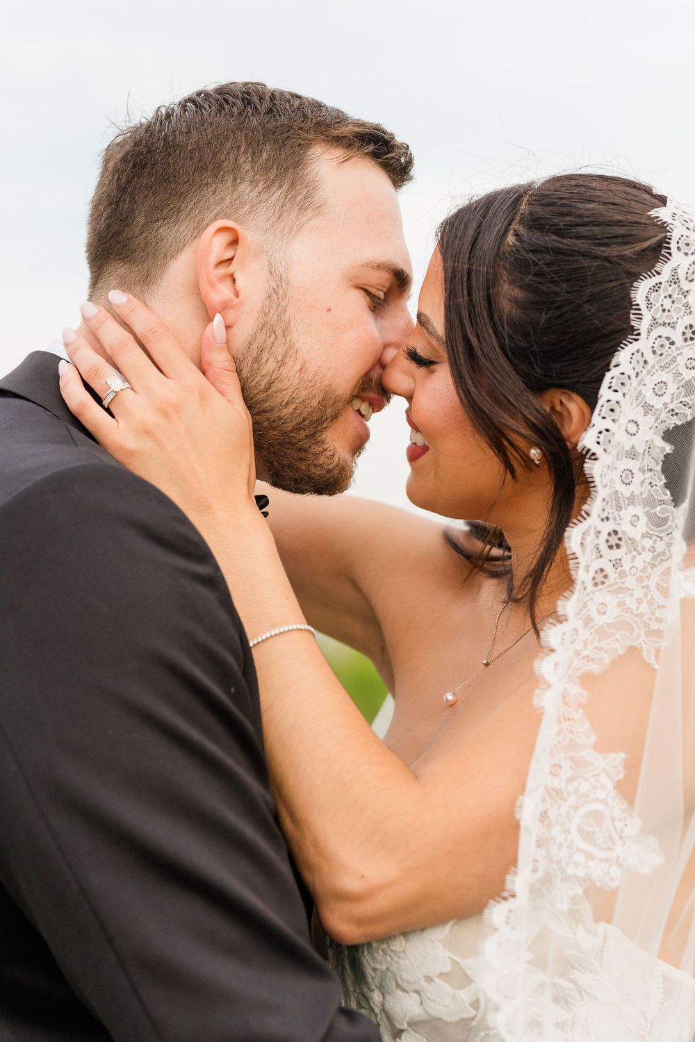 Close-up of bride and groom almost kissing, bride wearing lace veil and pearl jewelry on their wedding day.