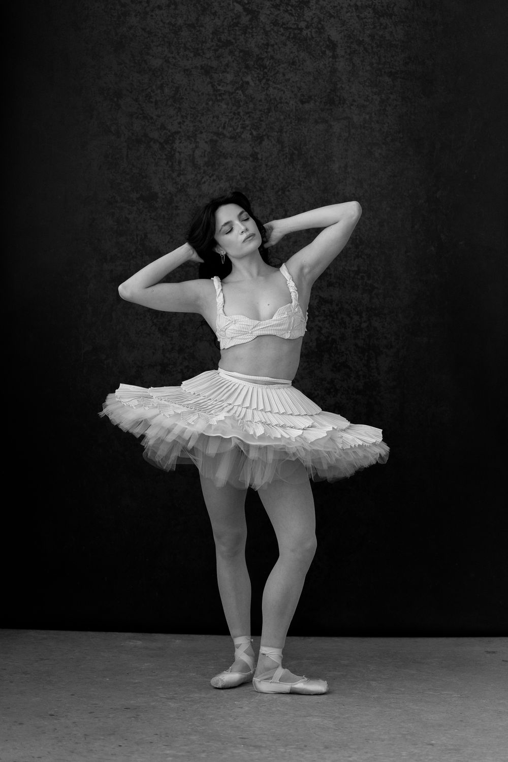 Black and white photo of ballerina in white tutu and pointe shoes posing gracefully in dance studio.