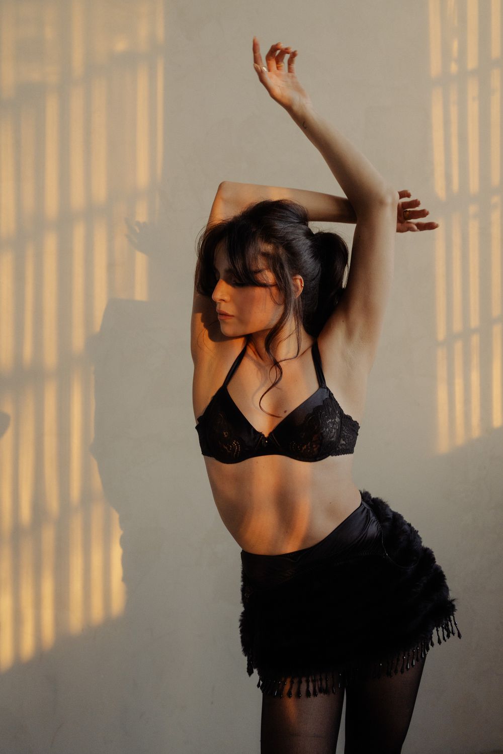 Woman in black lace bra and mini skirt dances with arms raised in golden sunlight.