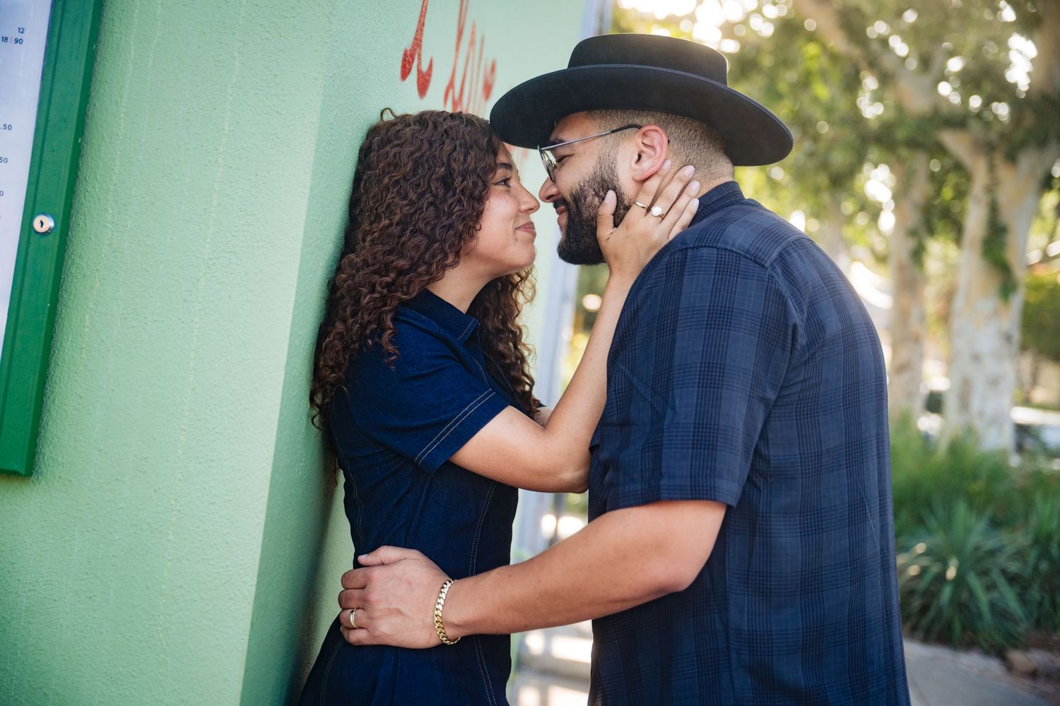 A couple sharing a romantic moment, the man in a cowboy hat and plaid shirt, the woman in a blue dress, outdoors.
