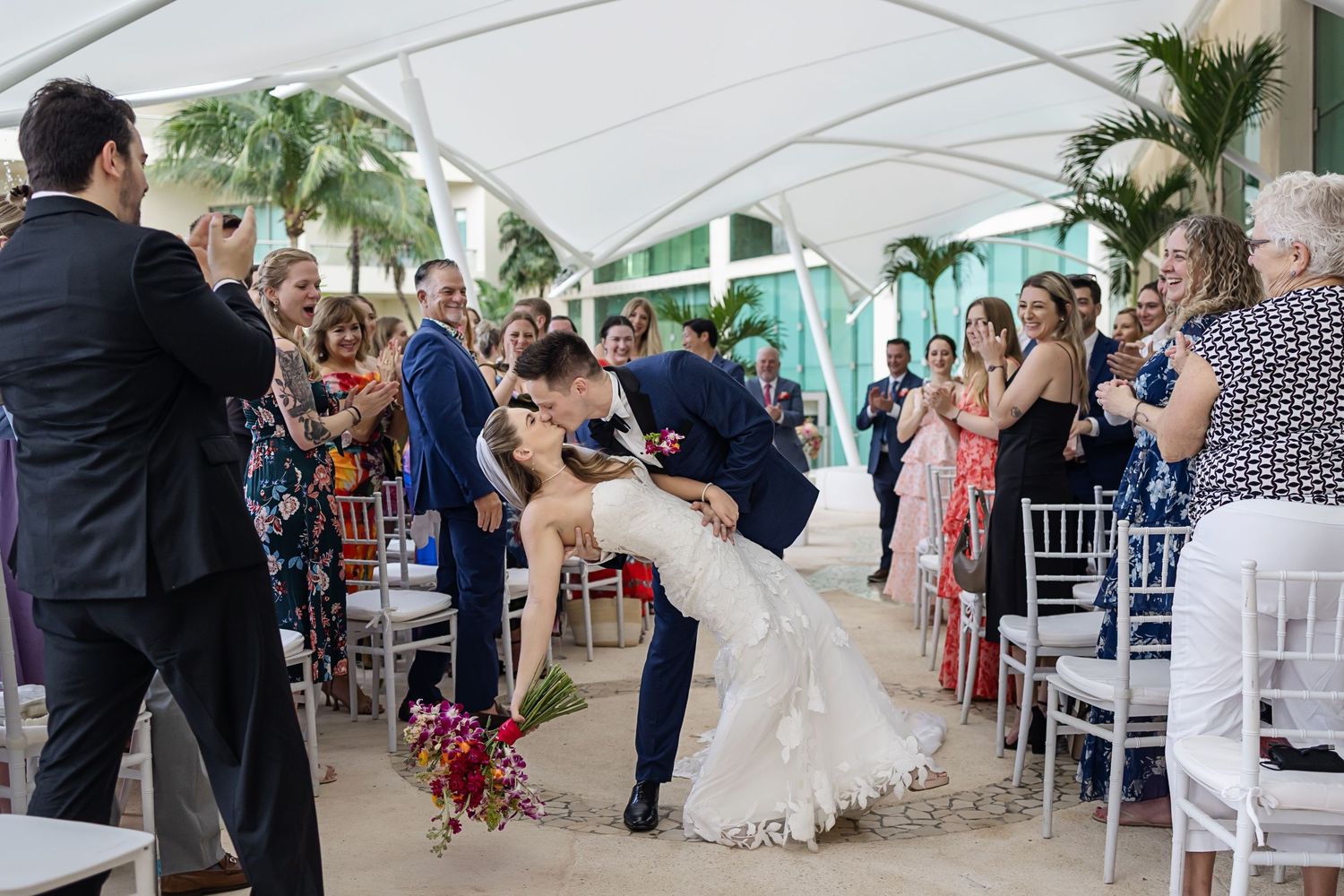 Bride and groom kiss joyfully during their ceremony exit at Live Aqua Cancún surrounded by cheering guests.