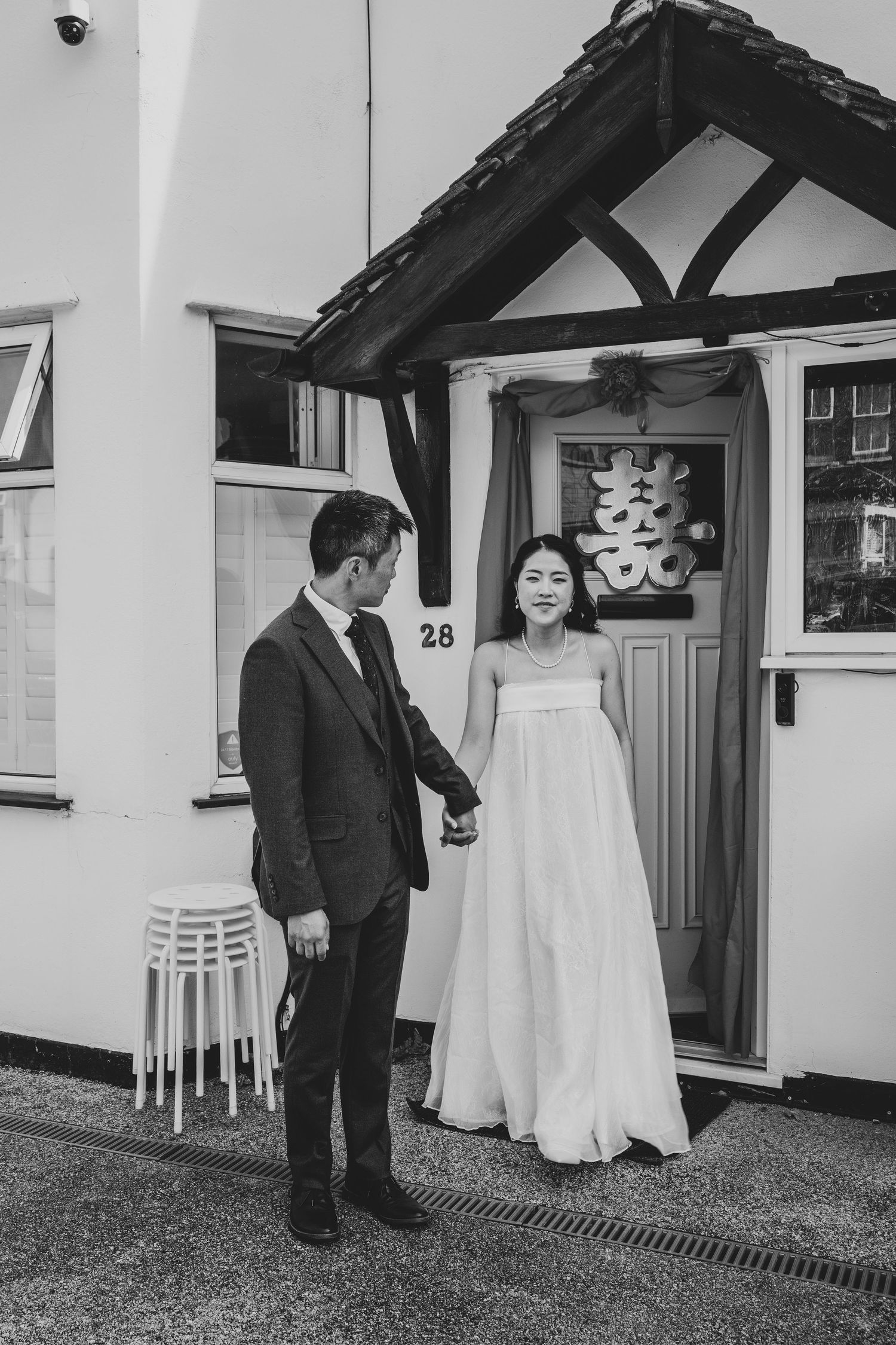 Bride and groom hold hands outside their home decorated with a Chinese double happiness symbol.