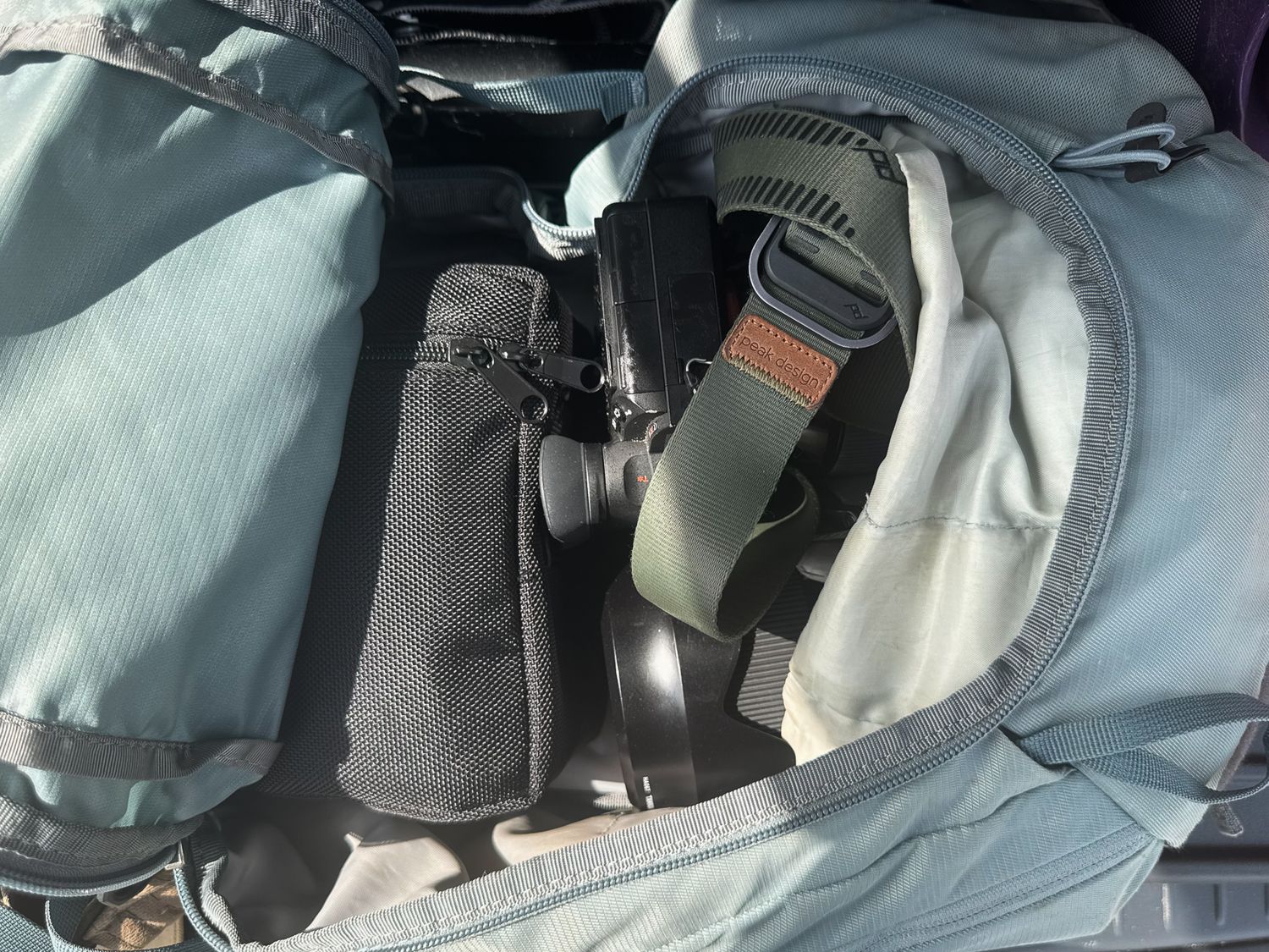 Close-up of a camera stored inside an open blue hiking backpack with straps and accessories.