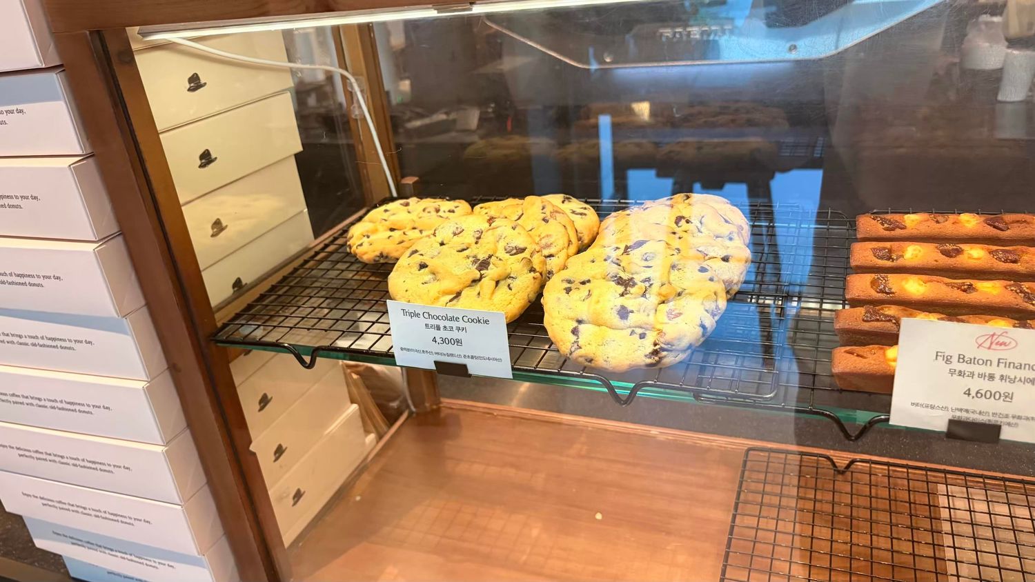 Glass bakery display case showcasing large chocolate chip cookies and pastries on wire cooling racks.