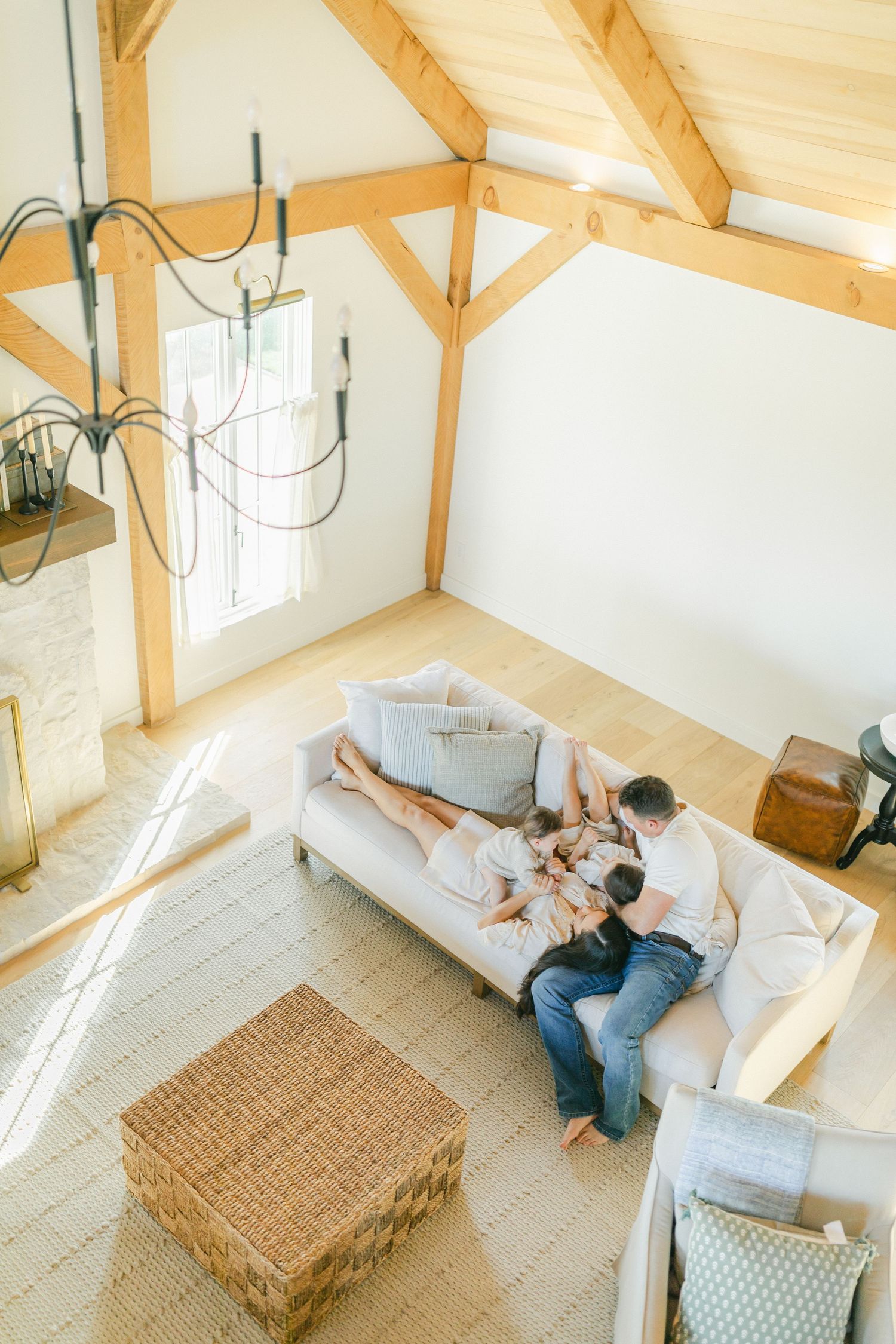 Aerial view of a family relaxing on a white sofa in a bright living room with wooden beam cathedral ceiling.