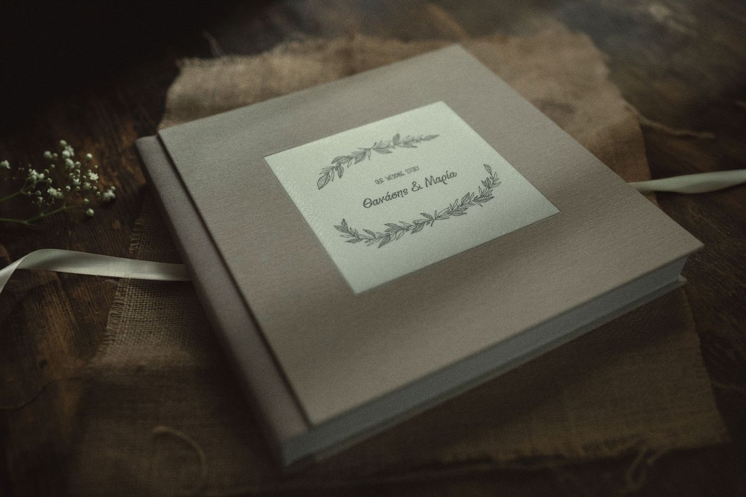 Rustic wedding photo book with a personalized fabric cover and custom botanical nameplate on a burlap background.