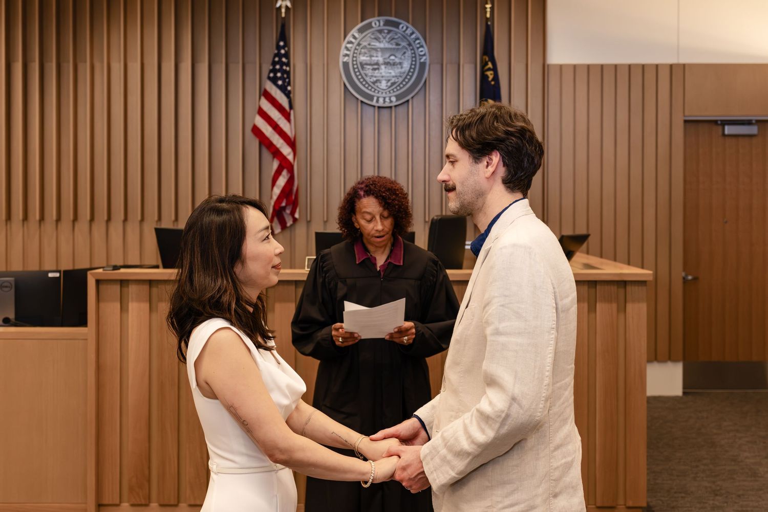 Couple exchanging vows at a courthouse wedding ceremony with a judge officiating in a wood-paneled courtroom.