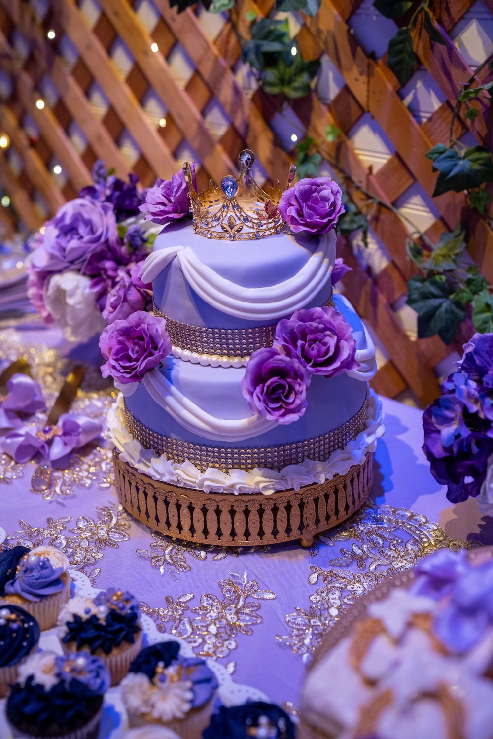 Elegant three-tier purple quinceañera cake with gold crown, purple roses, and decorative draping.