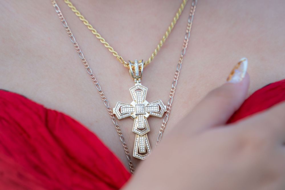 Gold cross pendant necklace with diamond accents layered on chains, worn by a woman in a red outfit.