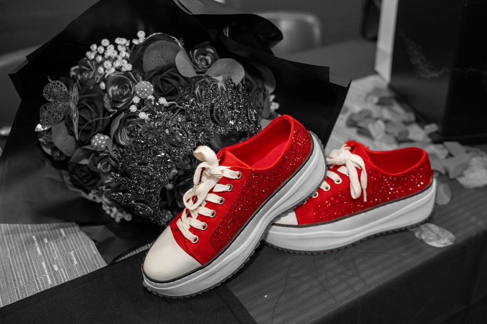 Red glitter sneakers with white laces and soles displayed next to a black bouquet on a monochrome background.