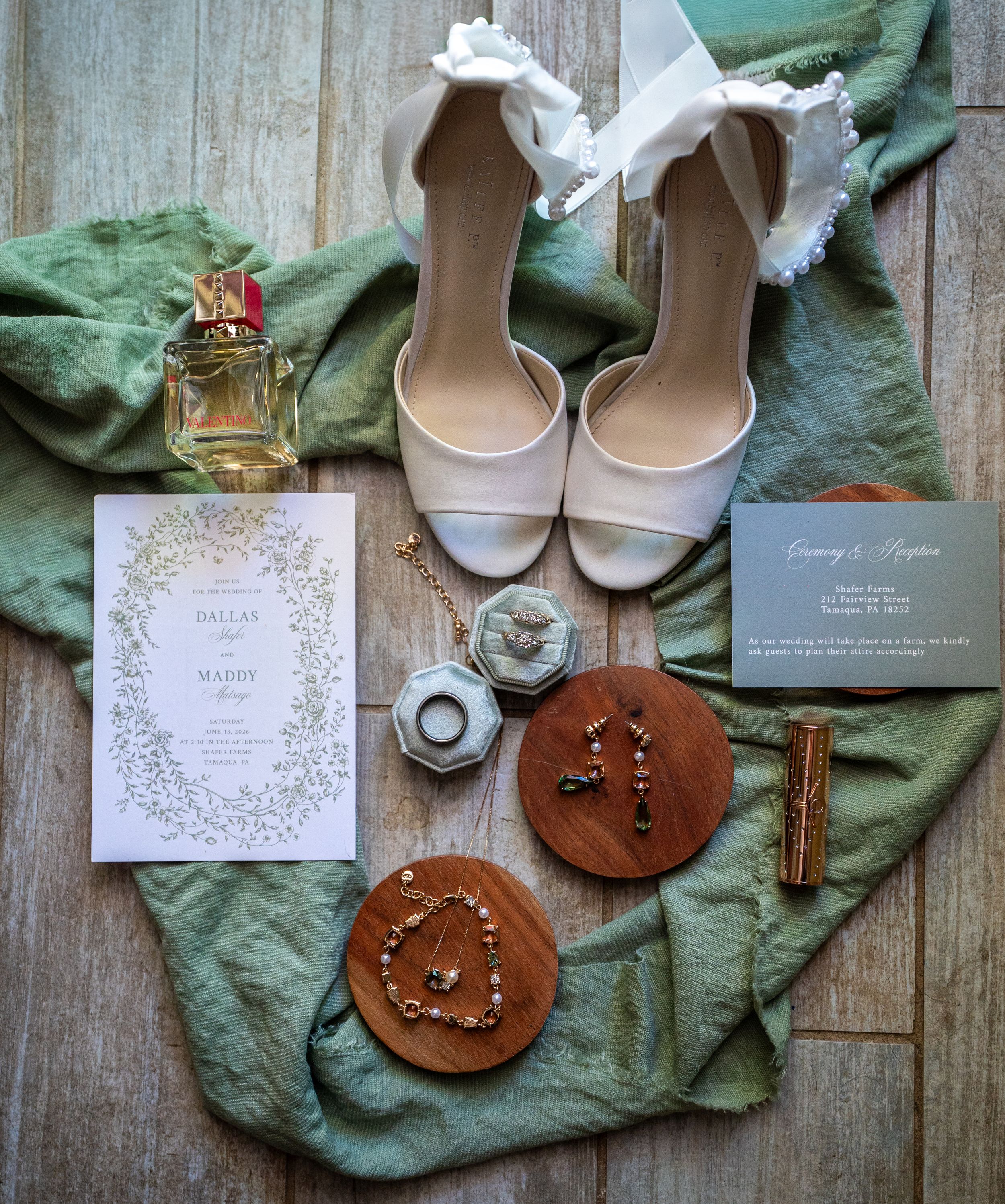 Elegant wedding flat lay with bridal heels, invitations, jewelry, perfume, and accessories on green linen fabric.