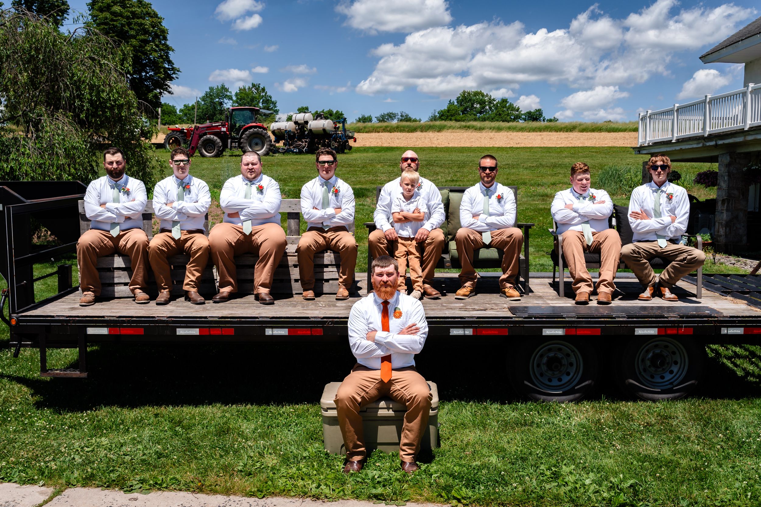 Groomsmen in matching white shirts and khaki pants posed on a flatbed trailer outdoors.