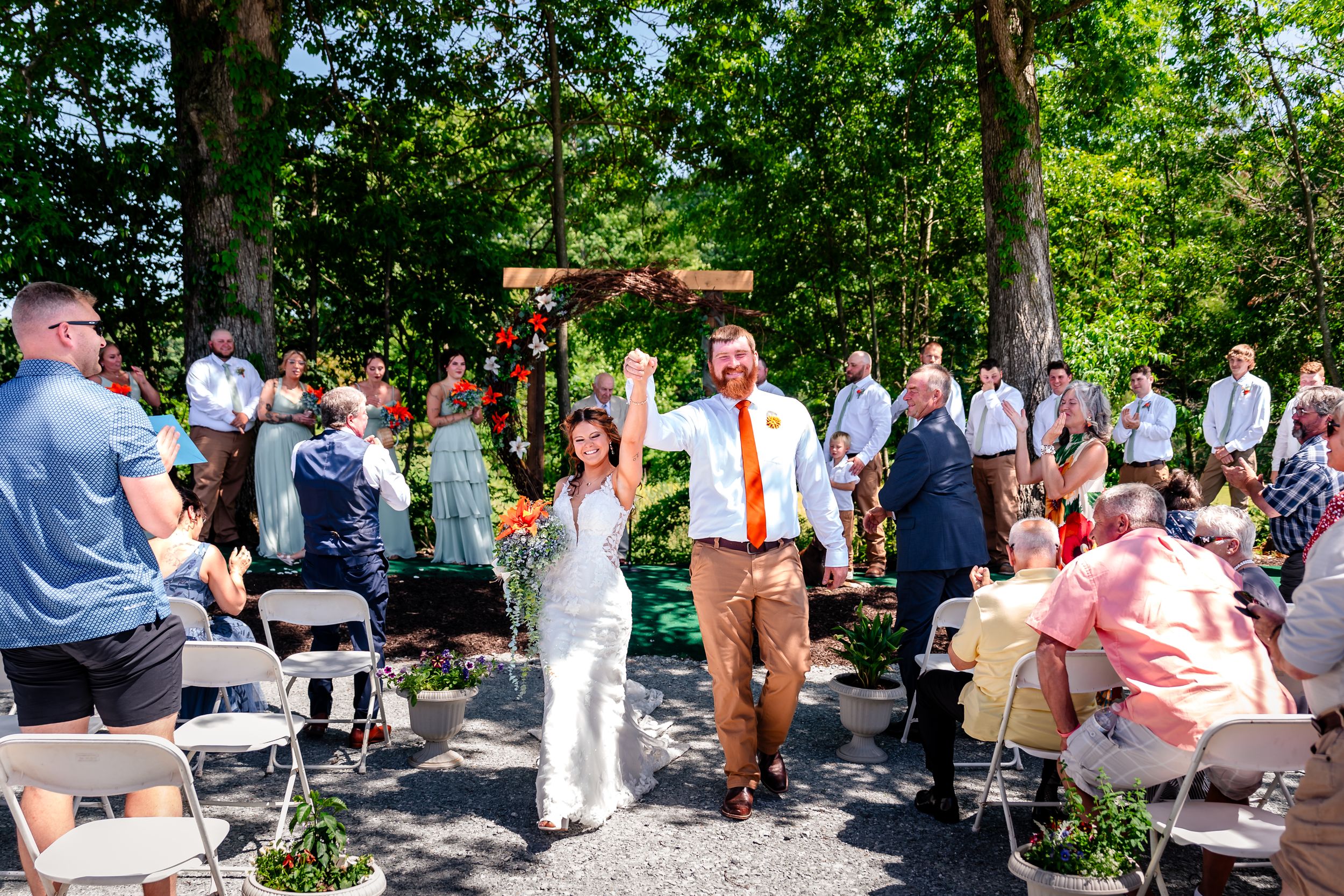 Newlyweds walk joyfully down the aisle after outdoor wedding ceremony as guests celebrate around them.