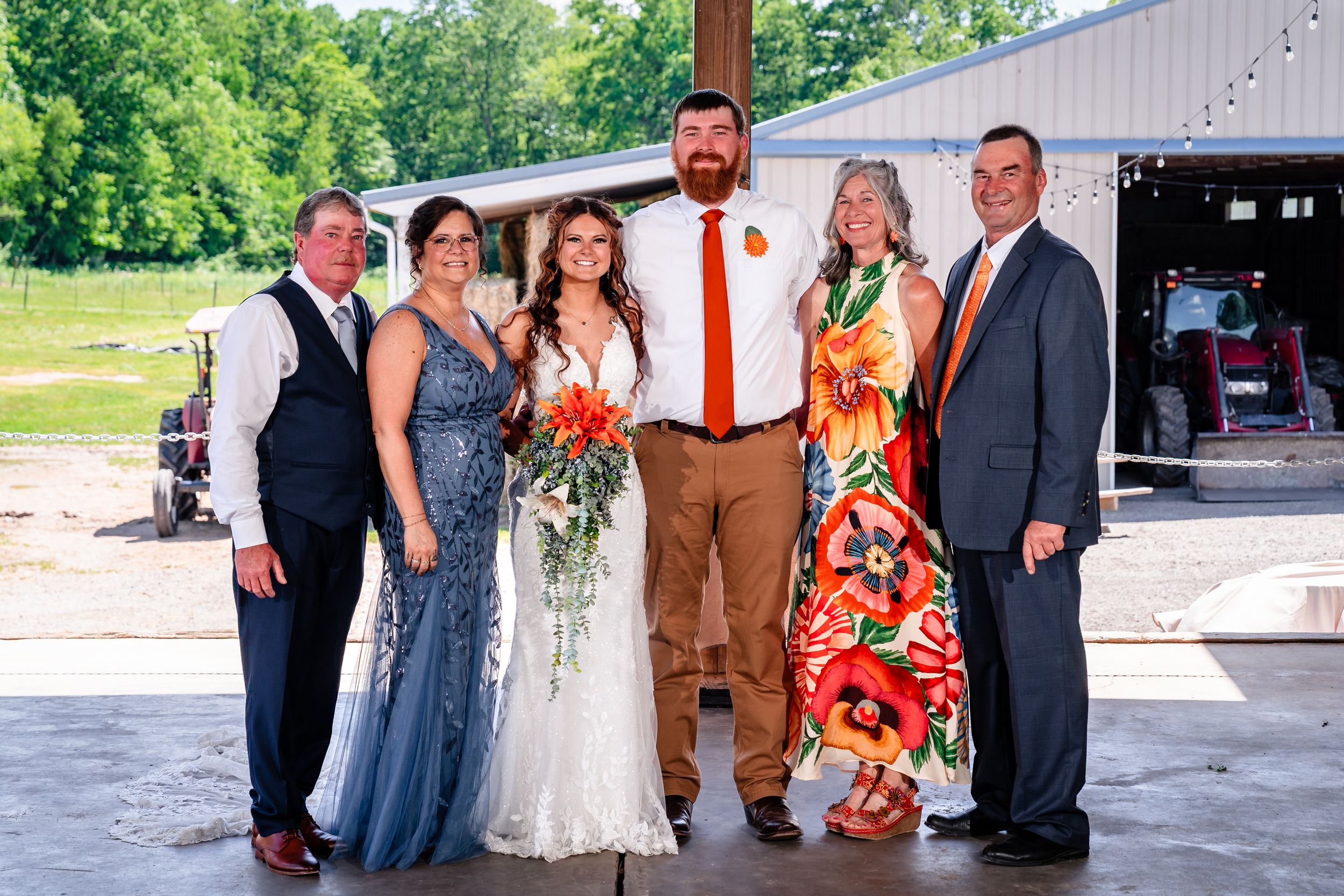 Wedding couple poses with family of four in front of barn at outdoor summer wedding.