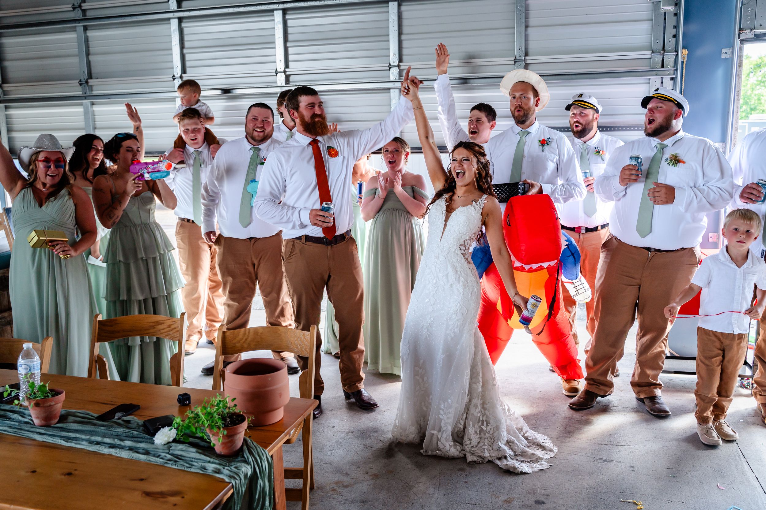 Excited wedding party cheers and celebrates inside a barn reception hall with the bride and groom.