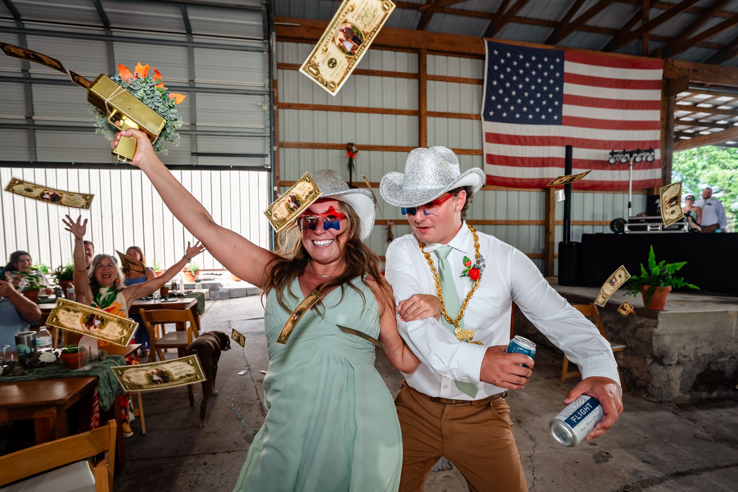 Wedding guests in cowboy hats dancing and throwing money at lively barn reception celebration.