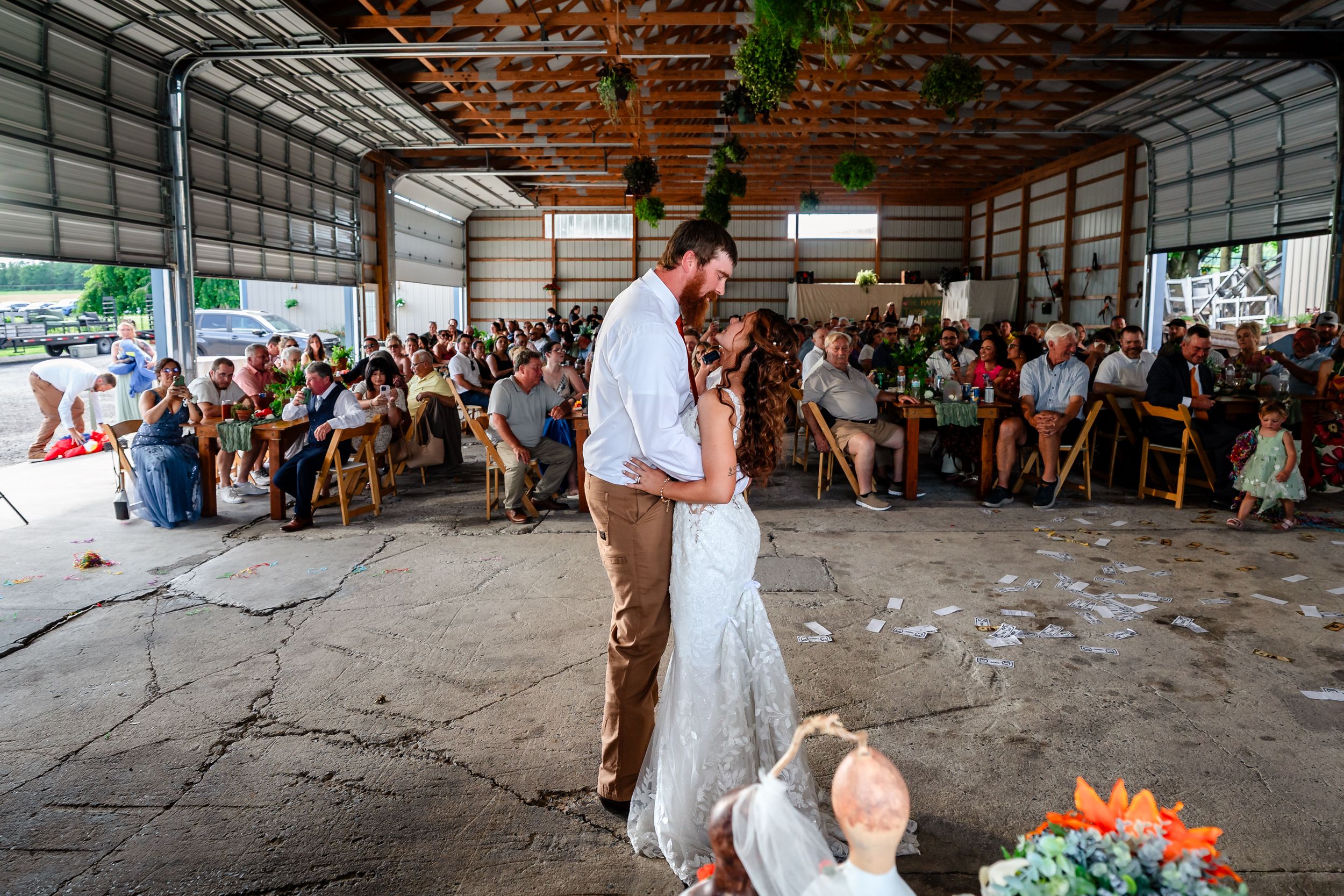 Bride and groom share first dance in rustic barn venue with large seated wedding crowd.