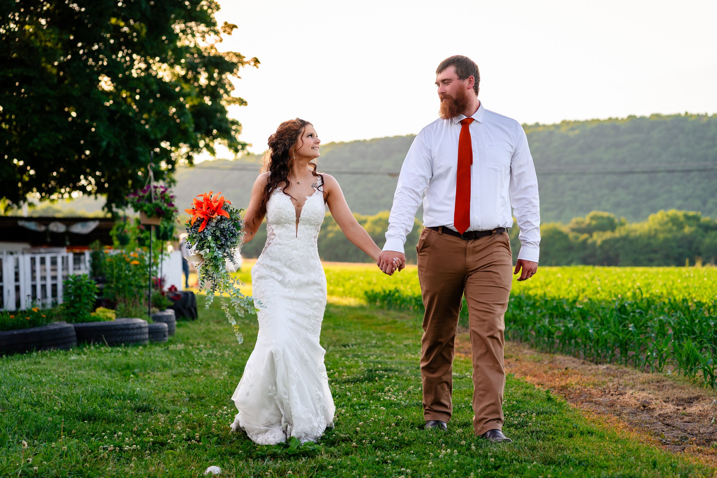 Bride and groom walking hand in hand through a green field at sunset on their wedding day.