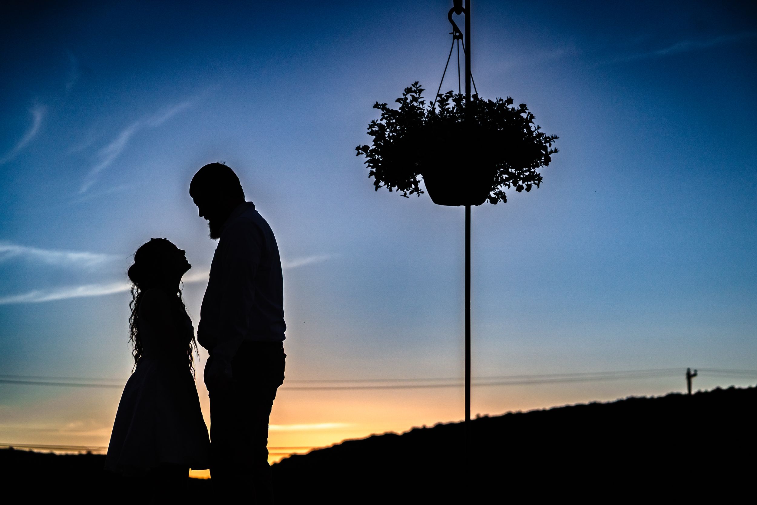 Romantic silhouette of a couple standing together at sunset with a hanging flower basket nearby.