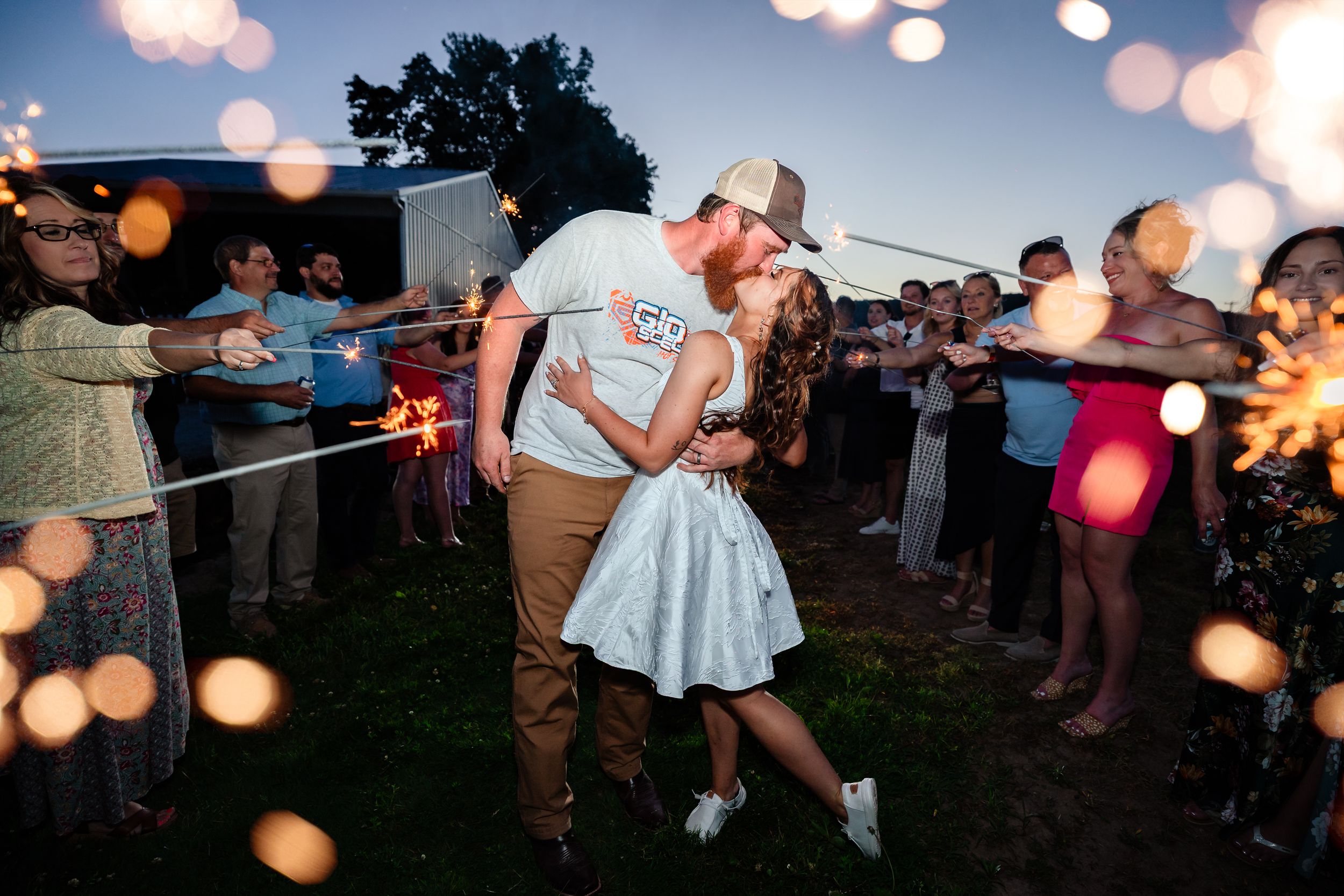 Couple shares a romantic kiss surrounded by sparklers during an outdoor evening wedding celebration.