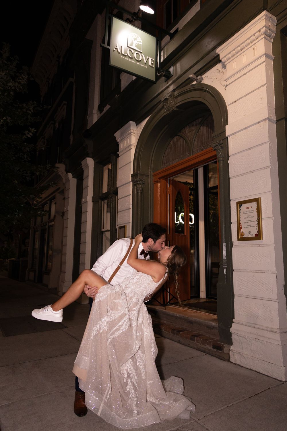 Groom dips bride in wedding attire outside the Alcove Cincinnati wedding venue at night in a romantic celebratory pose.