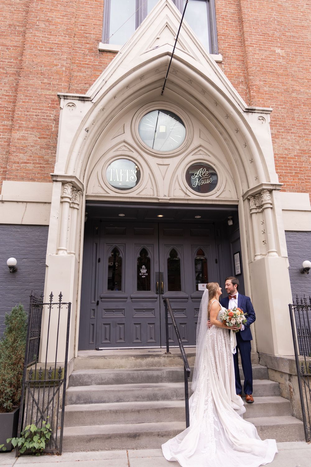 Bride and groom share a romantic moment on the steps of a historic brick church with Gothic arched doorway.