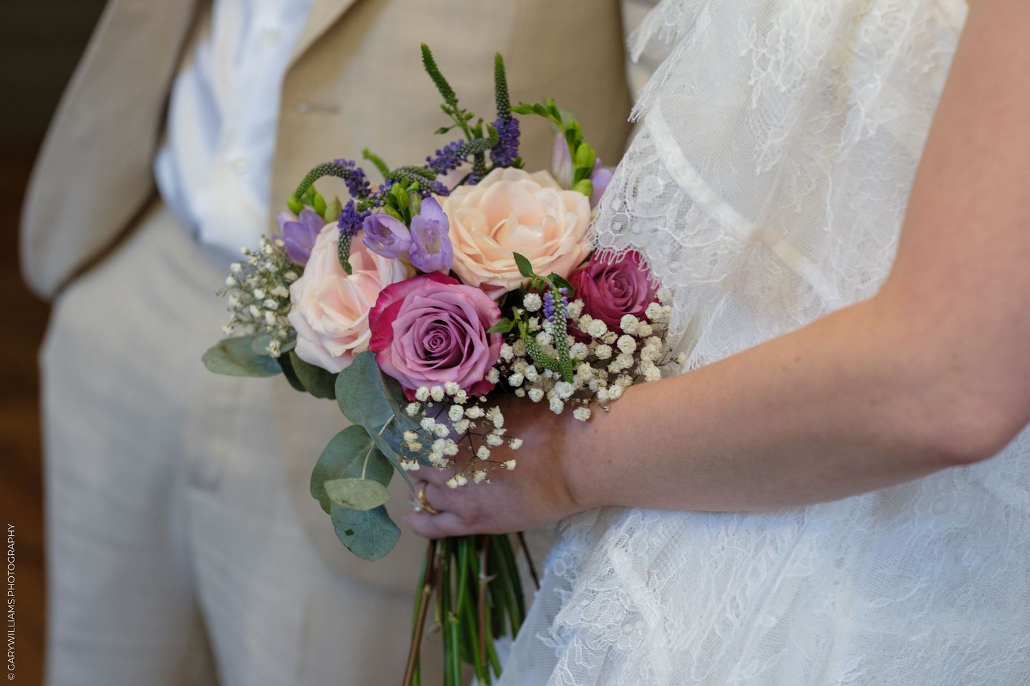 Bride holding a colorful wedding bouquet with pink and purple roses and baby's breath.