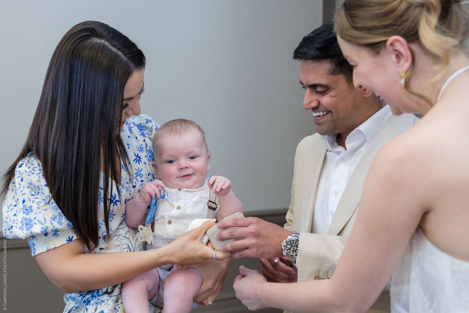 A woman holds a baby while a man and another woman interact with the infant at a family gathering.