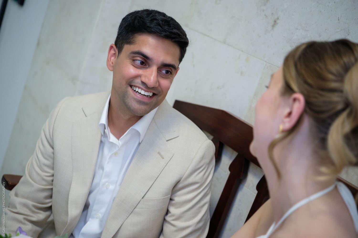 A smiling man in a beige suit converses with a blonde woman at a formal event.