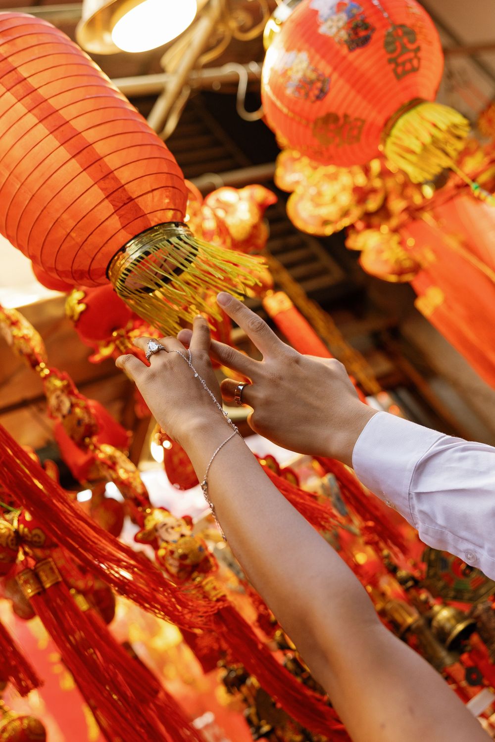 Hands touching red Chinese lanterns and gold decorations during Lunar New Year celebrations.
