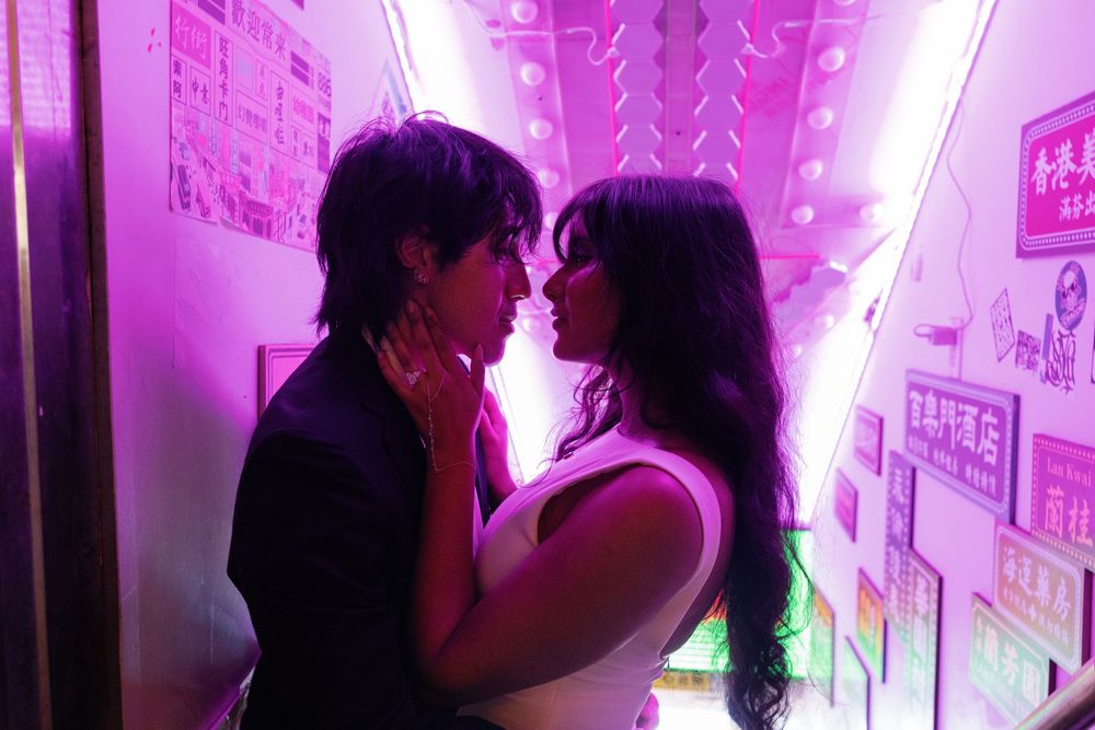 Couple sharing a romantic moment in a neon-lit pink corridor with Asian signage in the background.