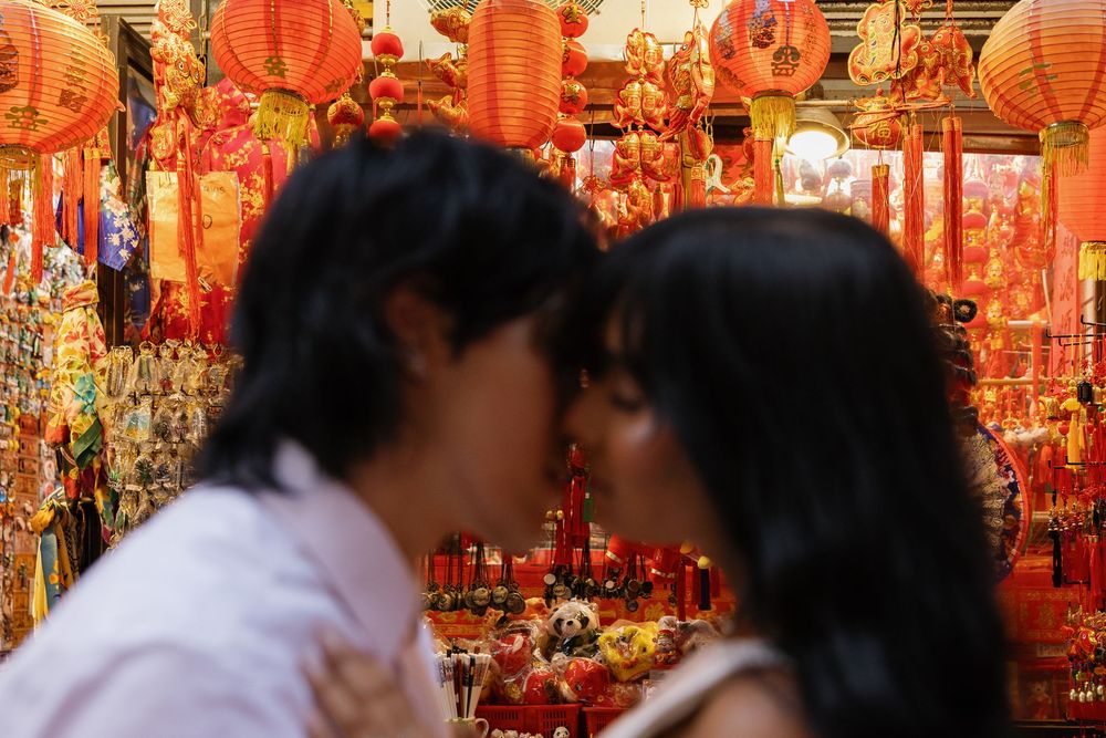 Couple kissing in front of vibrant red Chinese New Year decorations and lanterns in a festive market.