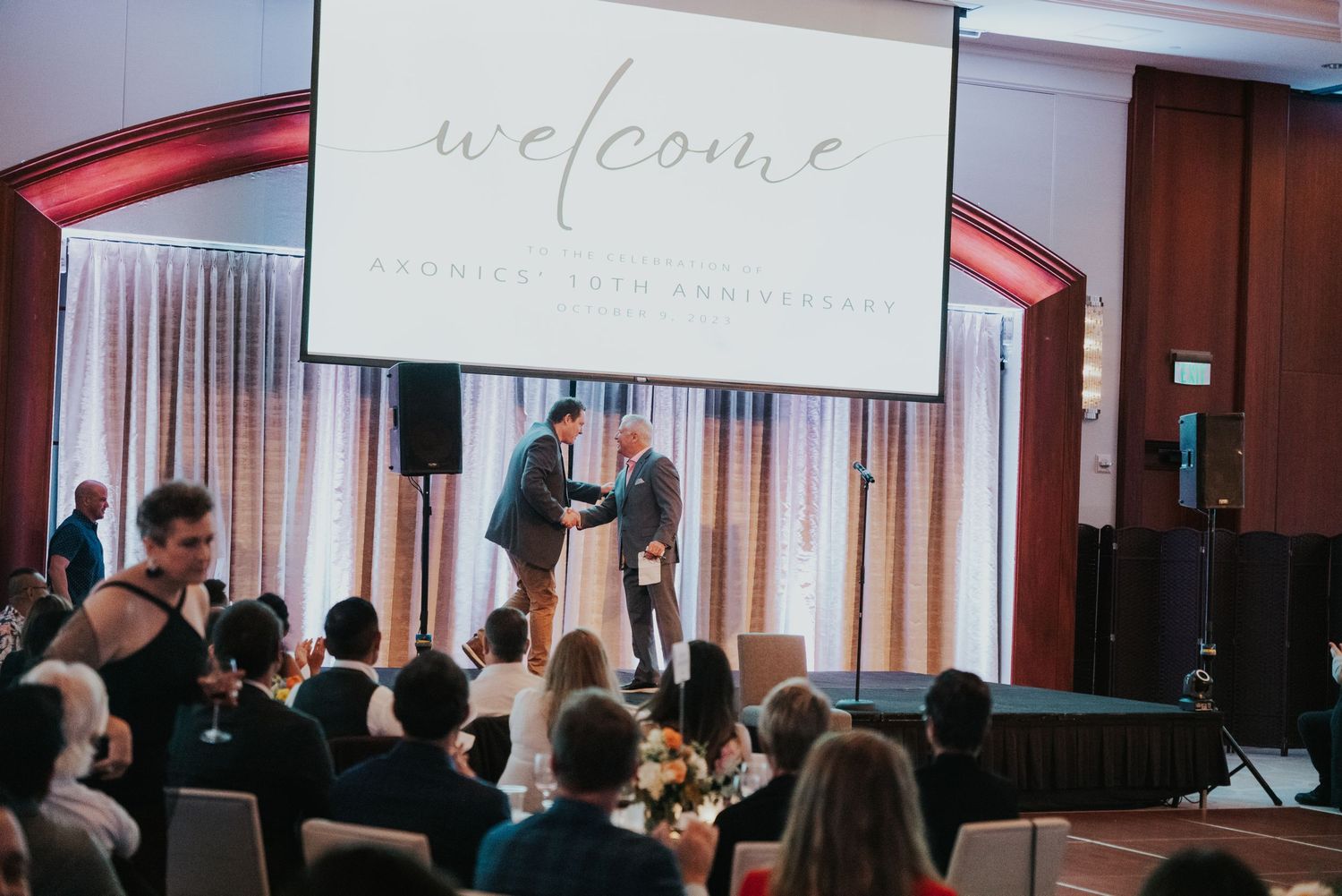 Couple celebrating wedding anniversary on stage with welcome sign at elegant venue reception.