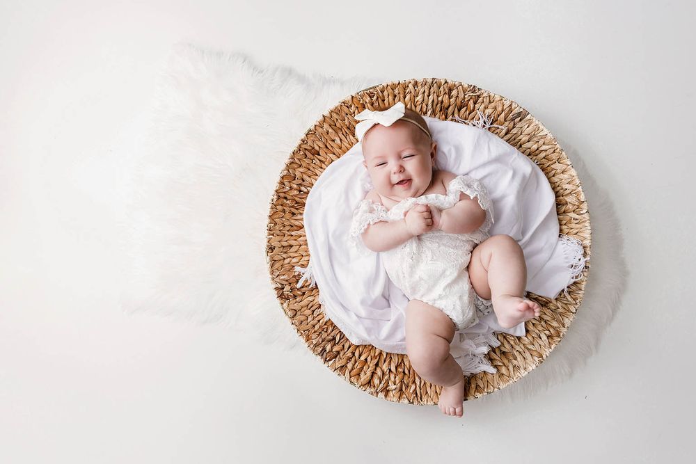 Smiling newborn baby lying in a woven basket with white fabric on a white background.