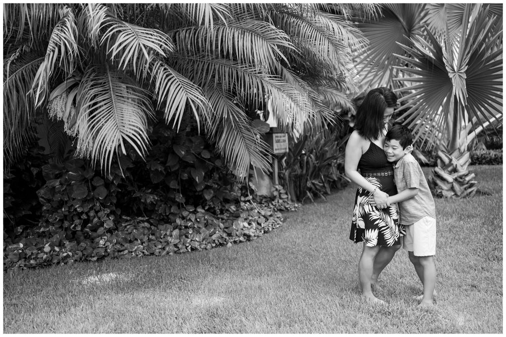Black and white portrait of a mother and child embracing in a tropical Punta Mita setting with palm trees and natural light.