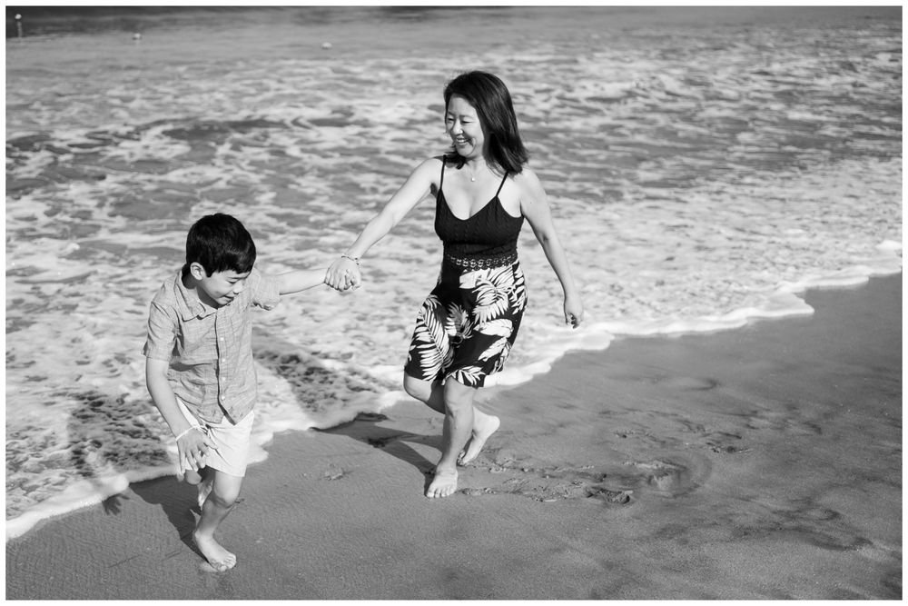 Black and white photo of a mother and son playing in ocean waves on a sandy Sayulita beach, Mexico, candid family photography.