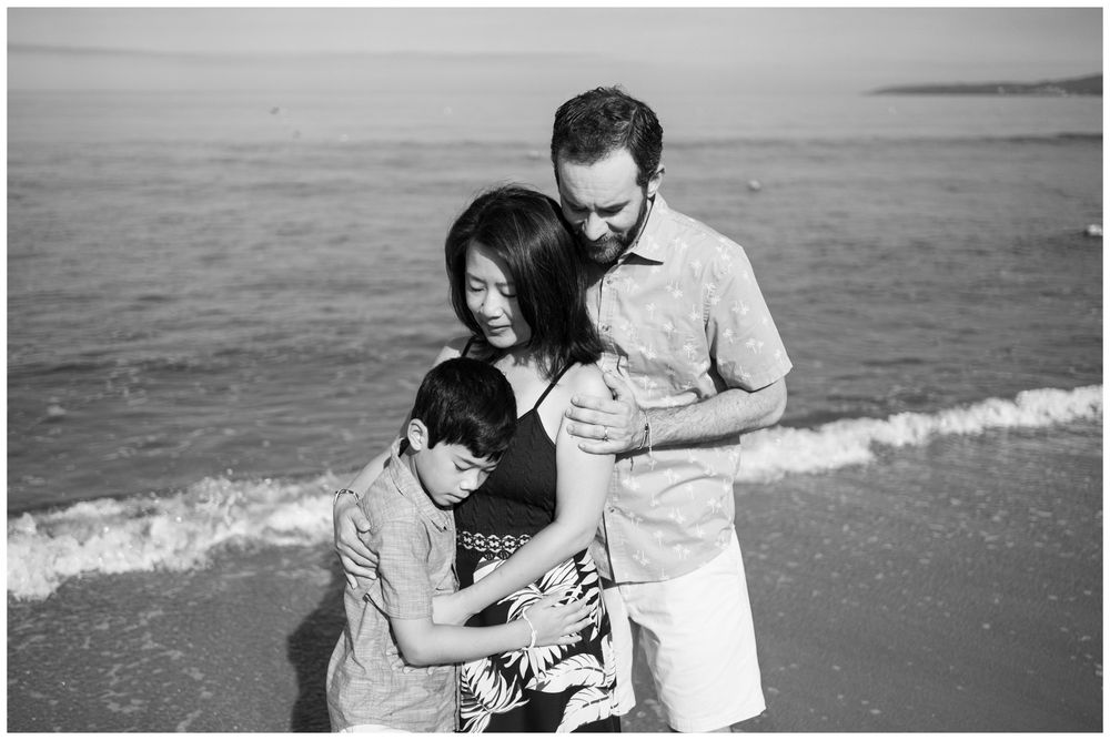 Family of three sharing a tender moment on Sayulita beach, Mexico in black and white, candid Riviera Nayarit family photography.
