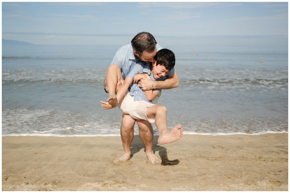 Father lifting child on Sayulita beach, Mexico with ocean waves, candid family photography Riviera Nayarit.