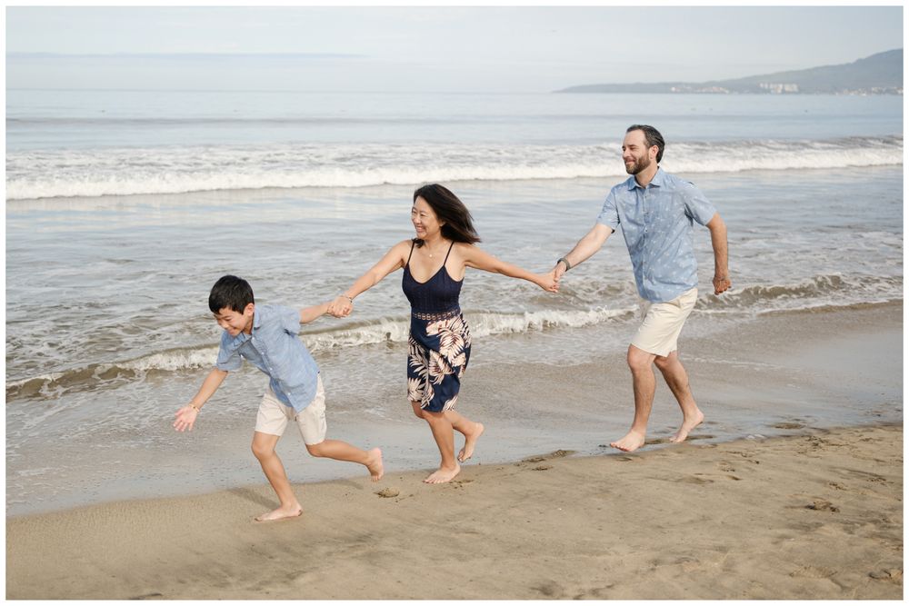 Family of three running on Sayulita beach in Mexico near ocean waves, sunny day candid family photography Riviera Nayarit.
