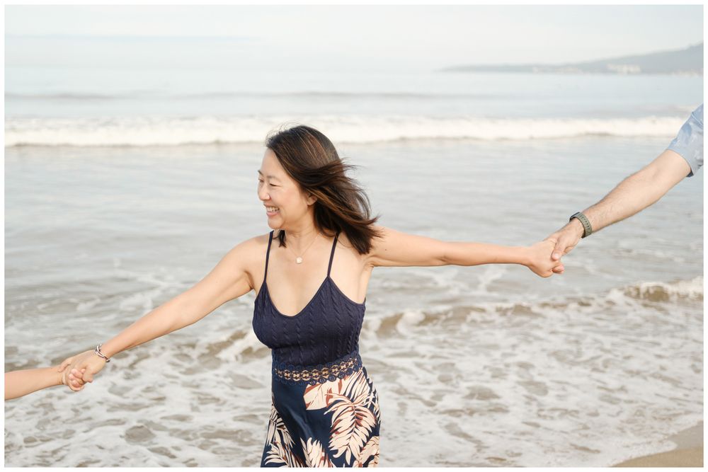 Woman smiling on Puerto Vallarta beach, arms outstretched holding hands, candid family beach photography Mexico near ocean waves.